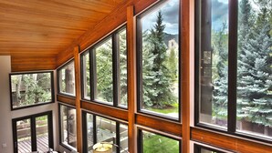Una habitación con ventanas amplias, techo de madera y vistas a árboles y una montaña.