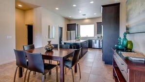 A modern kitchen with dark cabinetry, a central island, and a dining area with a large table and chairs.