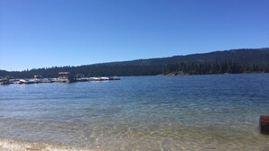 Un lago tranquilo con barcos amarrados en la orilla y una colina boscosa al fondo.