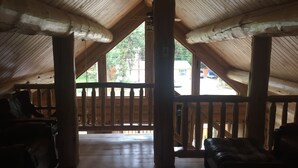 Habitación en ático con vigas y baranda de madera, y vista al exterior.
