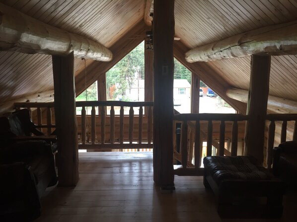 Habitación en ático con vigas y baranda de madera, y vista al exterior.