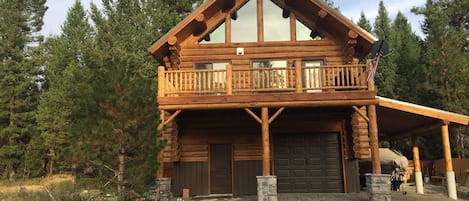 Une cabane en rondins avec un balcon, un garage et des fondations en pierre.