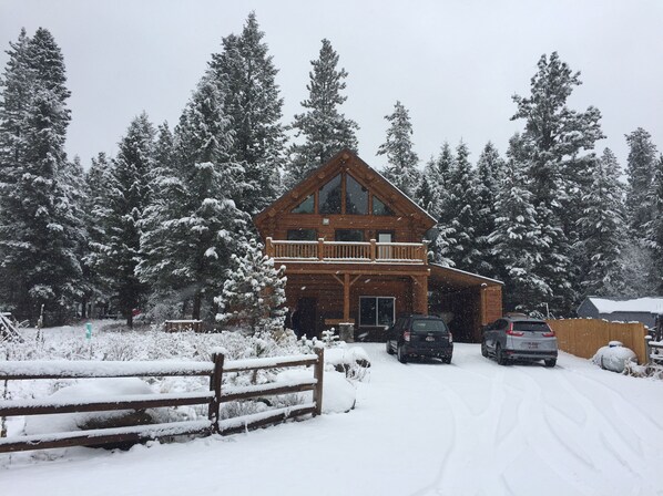 A two-story log cabin with a balcony, surrounded by snow-covered trees.