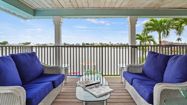 A covered outdoor seating area with wicker furniture and blue cushions, overlooking a body of water and palm trees. - Pool, Spa, Kayaks, Bikes, Fishing Gear & More waterfront, Amenities at no charge (Cape Coral)