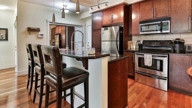 A modern kitchen with wooden cabinets, stainless steel appliances, and a central island with bar stools. - Modern open concept, close to DT and Free UG Parking. Discounted Monthly Rate. (Calgary)