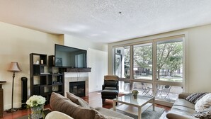 A modern living room with a large window, a flat-screen TV, a fireplace, and a comfortable seating area. - Modern open concept, close to DT and Free UG Parking. Discounted Monthly Rate. (Calgary)