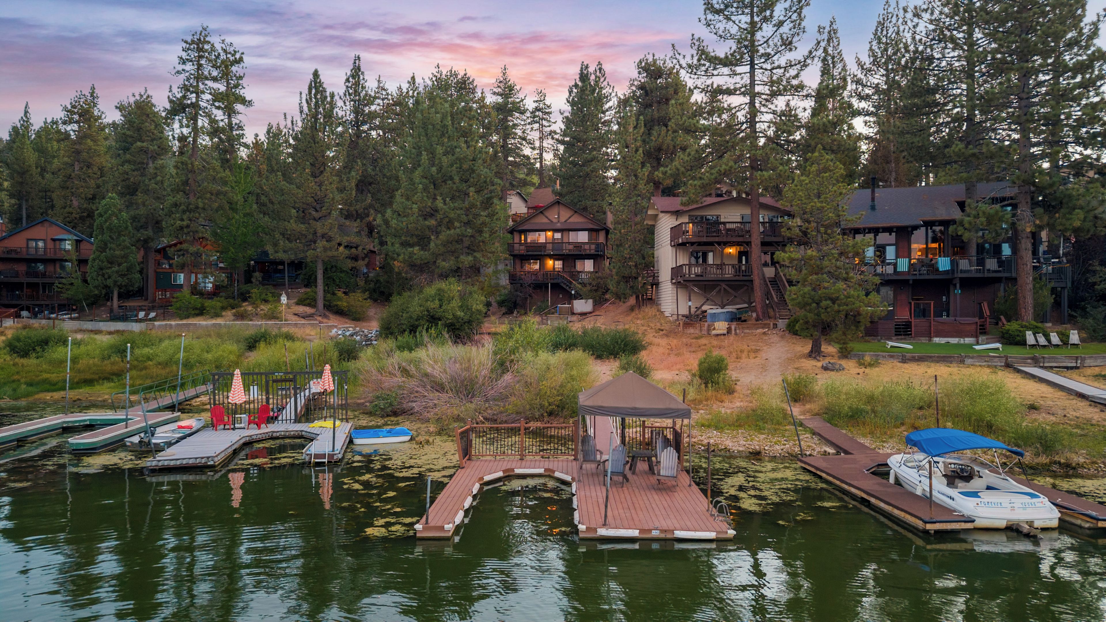 Une propriété au bord du lac comprenant plusieurs chalets, un quai avec des bateaux et un petit pont reliant les chalets.