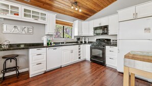 Una cocina moderna con armarios blancos, una estufa negra y techo de madera.