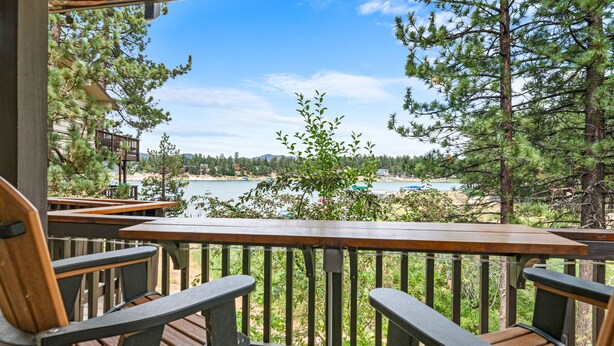 Terraza de madera con sillas que da a un lago y una playa.