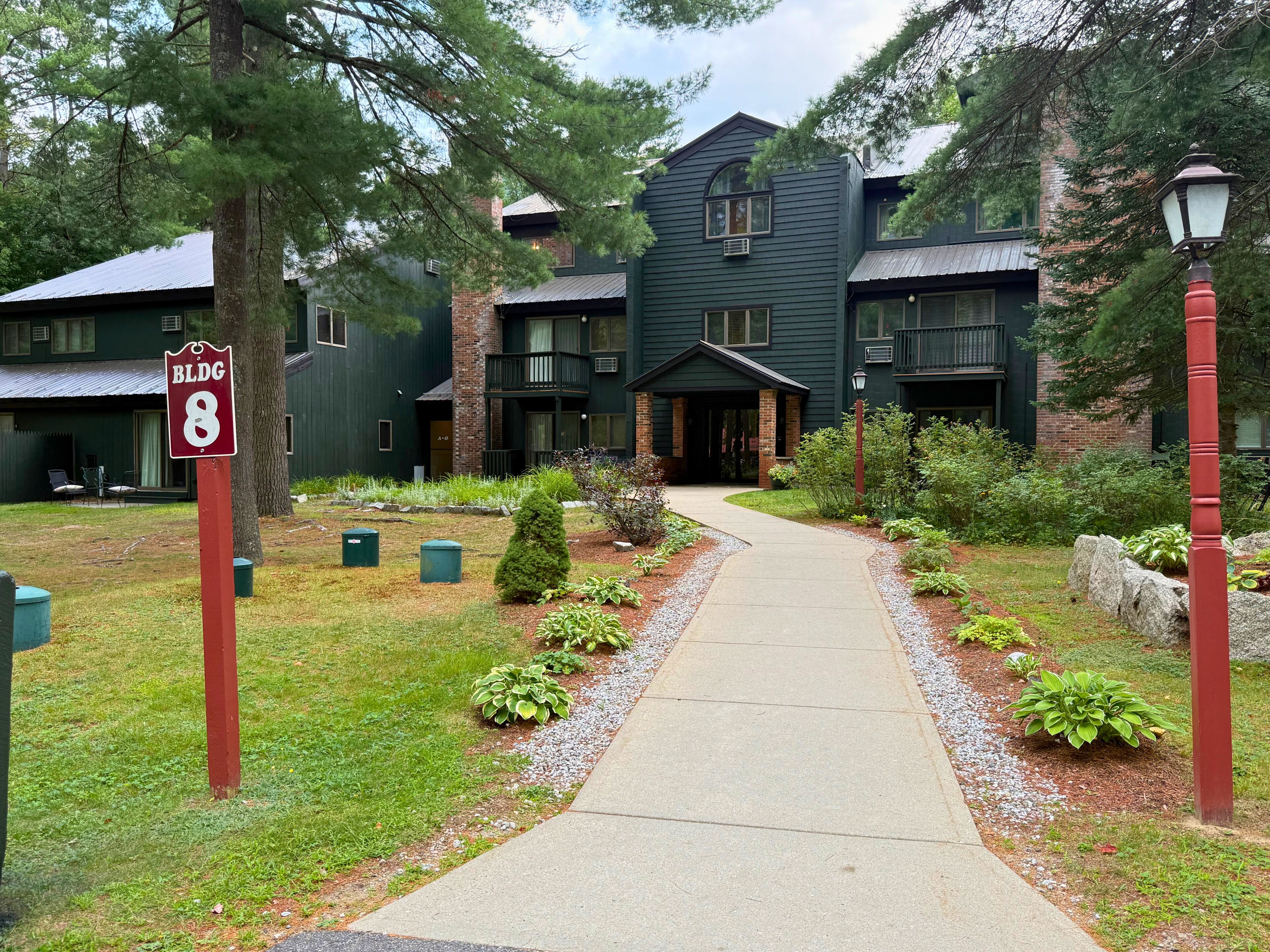 A building with a green exterior, a covered entrance, and a pathway leading to the entrance.