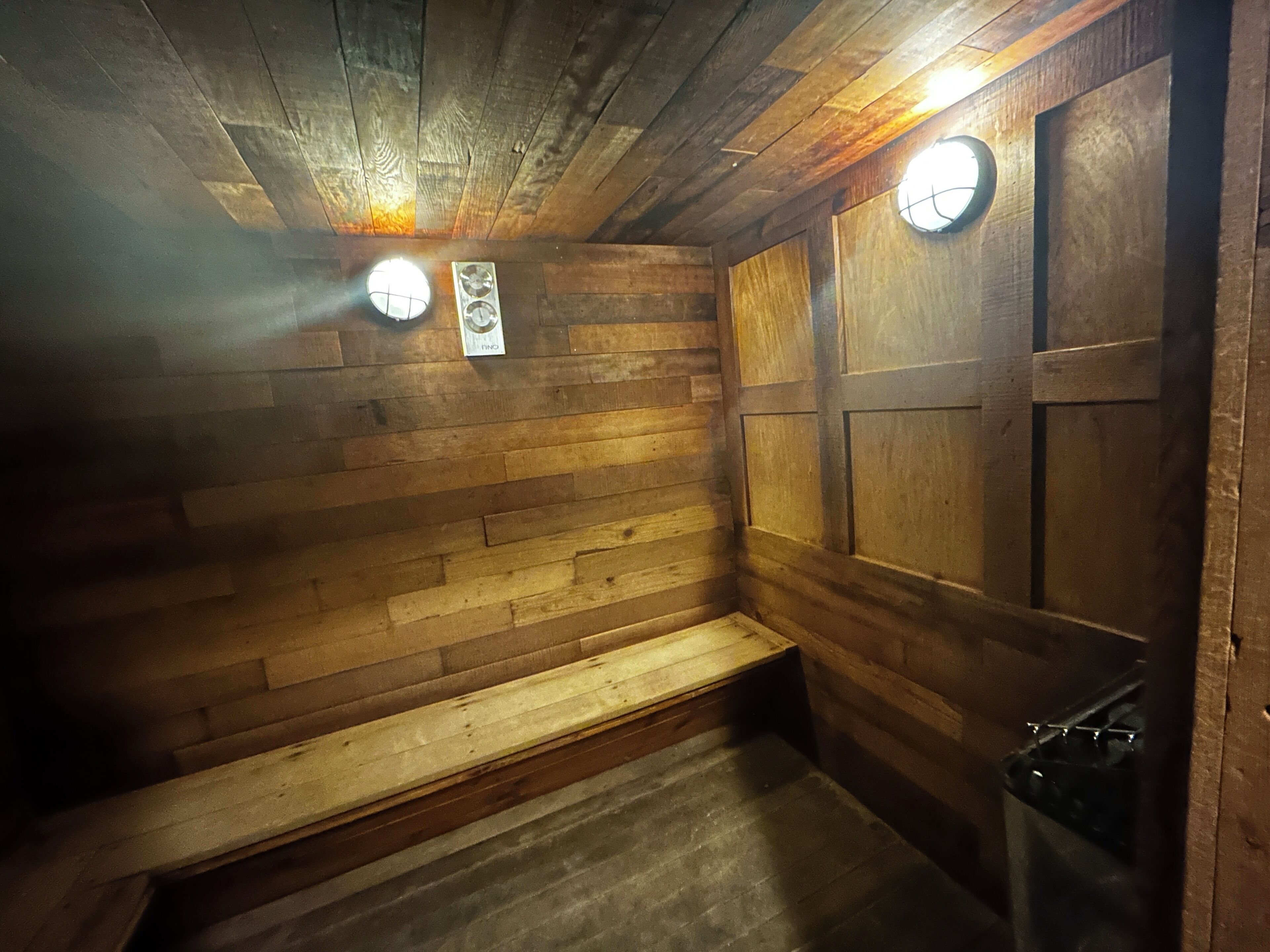 Een sauna met houten wanden, een bankje en twee wandlampen.