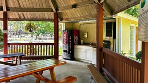 Un área de picnic techada con bancos de madera y un refrigerador Coca-Cola.
