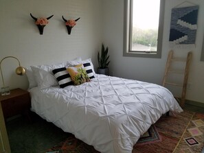 Une chambre avec un lit blanc, deux cornes décoratives accrochées au mur, une plante en pot et une échelle.