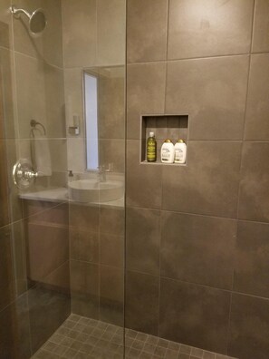 Een douchegedeelte met een glazen deur, een wastafel en een plank met toiletartikelen.