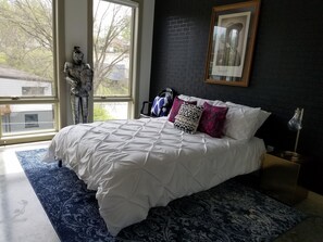 Een slaapkamer met een groot bed, een donkere bakstenen muur, een ingelijst kunstwerk en uitzicht op de omgeving.