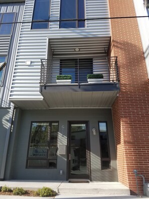 Een meerlaags gebouw met een begane grond ingang, een balkon met hekwerk en een gevel van baksteen.