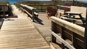 Ein hölzerner Steg führt zu Strandstühlen und Picknicktischen, wobei ein 'No Trace'-Schild sichtbar ist.