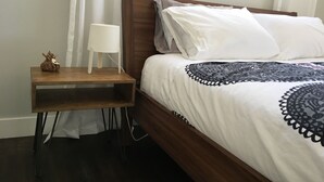 Ein ordentlich bezogenes Bett mit einer gemusterten Tagesdecke, einer Nachttischlampe und einem kleinen Nachttisch aus Holz mit einem dekorativen Gegenstand.