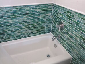 Une salle de bain avec une baignoire blanche, des carreaux de mosaïque verts et un robinet chromé.