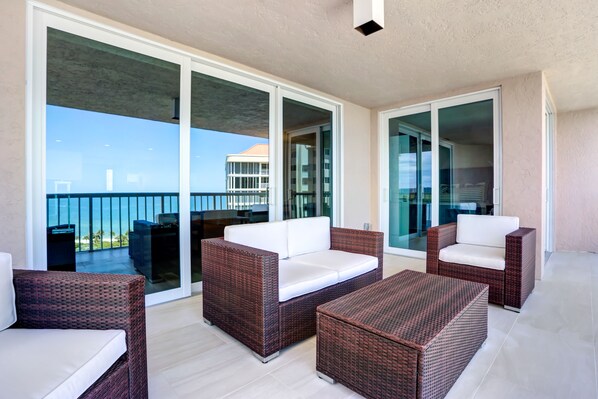 A balcony with wicker furniture and glass doors leading to a terrace with a view of the ocean.