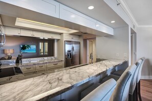 A modern kitchen with a marble countertop, built-in appliances, and a seating area with cushioned chairs.