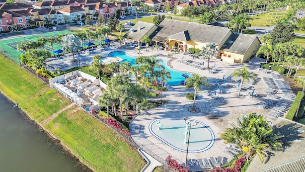 Luchtbeeld van een resort met een centraal gelegen zwembad, ligbedden en een tennisbaan.