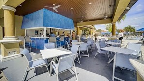 Un espace extérieur aménagé avec des tables et des chaises, un coin bar et une piscine en arrière-plan.