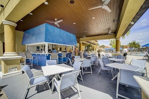 An outdoor patio area with tables and chairs, a bar area, and a pool in the background. - Stunning 5 Bedroom townhome in prime location- Paradise Palms resort community! (Kissimmee)