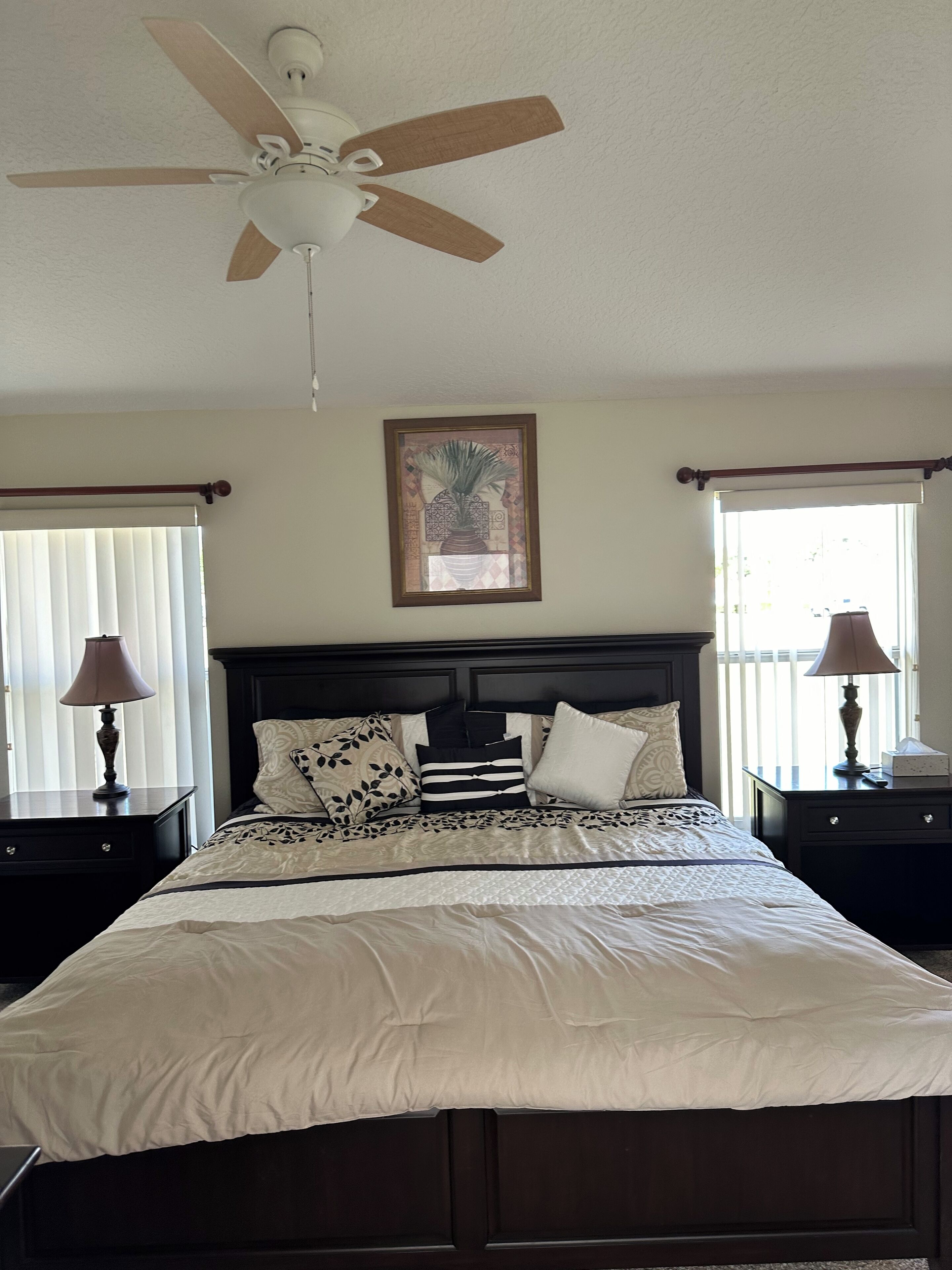 A bedroom with a bed, a ceiling fan, a framed artwork, bedside tables, and lamps.