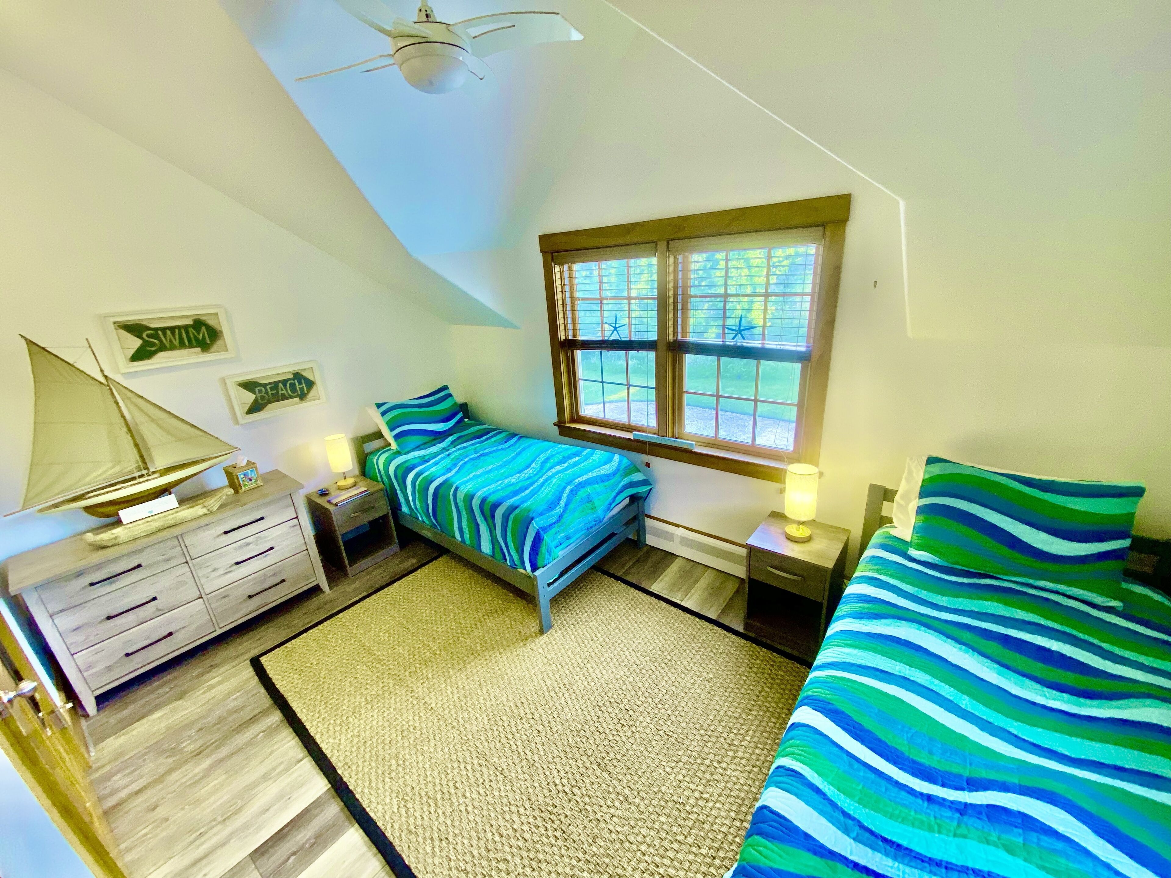 A bedroom with a bed, a nightstand, a dresser, a sailboat model, a window, and a ceiling fan.