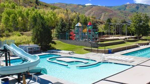 Ein Schwimmbecken mit Wasserrutsche, ein Spielbereich für Kinder und Blick auf eine Berglandschaft.