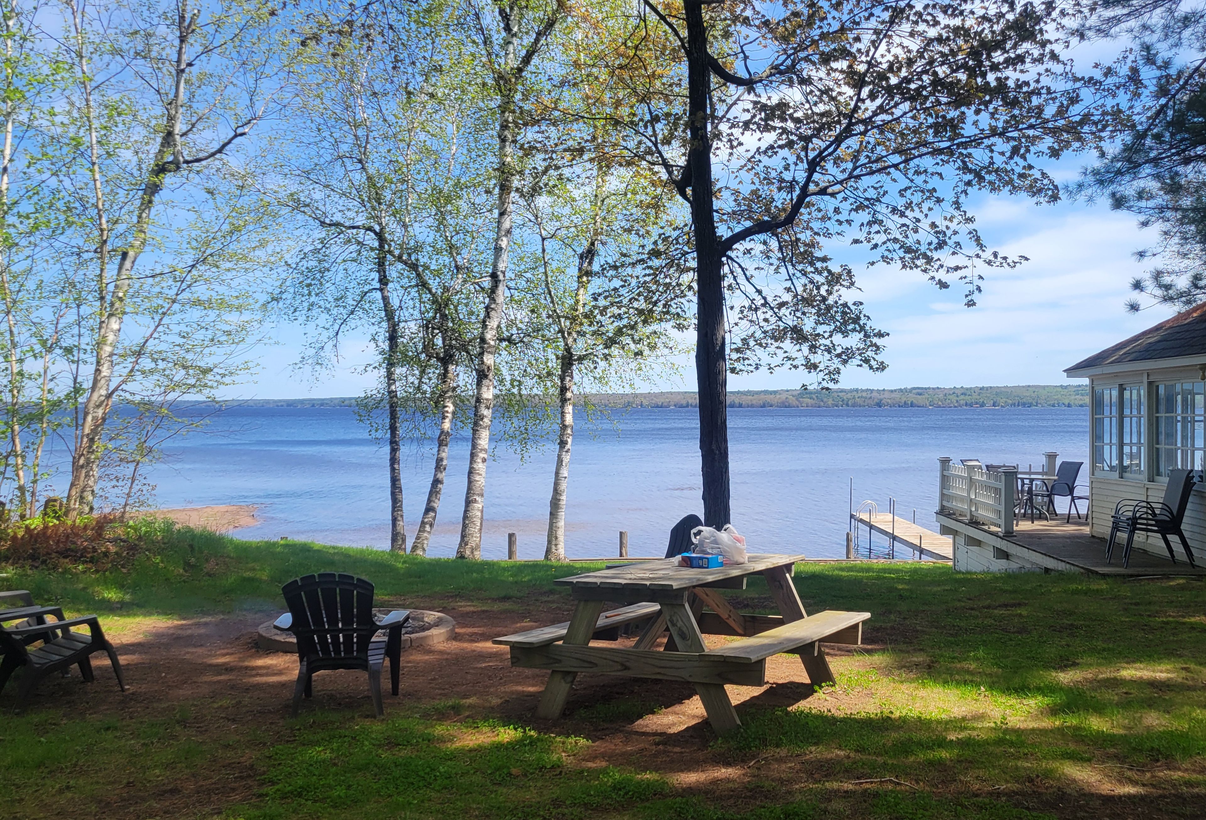 A lakeside patio with a wooden table and chairs, a covered seating area, and a view of the lake.
