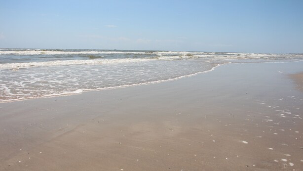 Ein Strand mit sanft anschwellenden Wellen unter blauem Himmel.