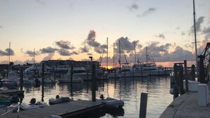 Ein Yachthafen mit Booten, die an Holzstegen liegen, umgeben von ruhigem Wasser und einem Sonnenuntergangshimmel.