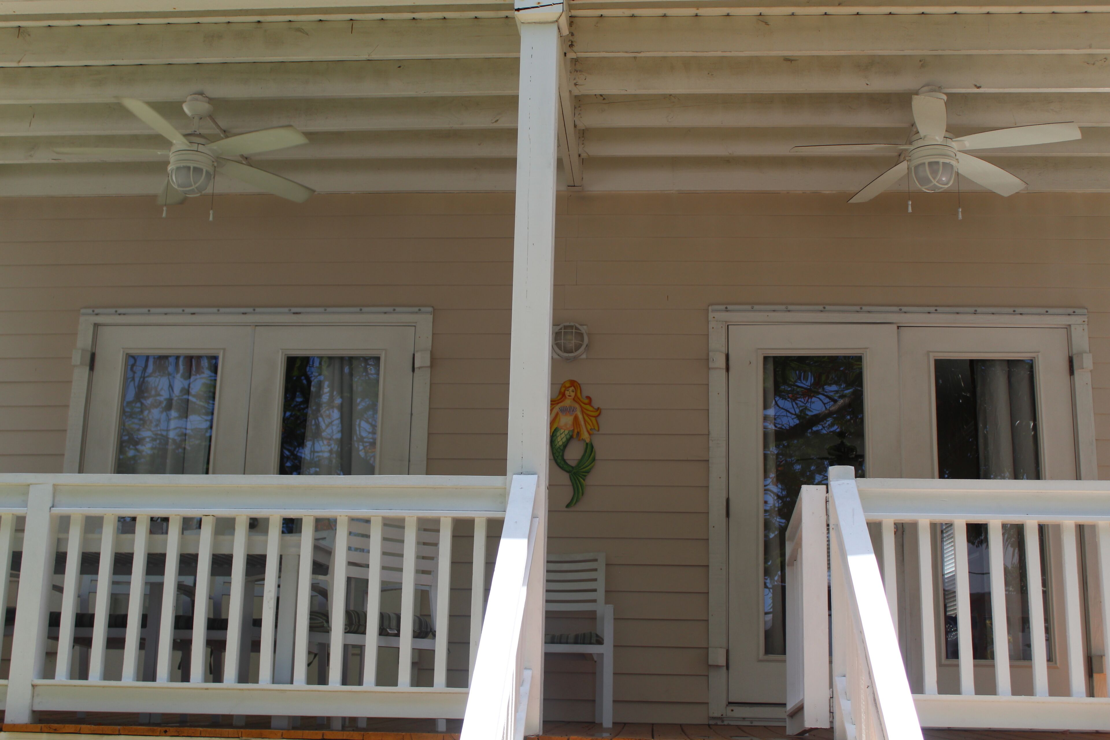 A porch with white railings, two ceiling fans, and a mermaid decoration on the wall.