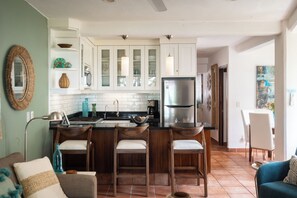 A modern kitchen with white cabinets, a stainless steel refrigerator, and a bar area with stools. - Coco Azul -Beach Front- Ocean Front-No Stairs (Puerto Vallarta)