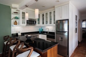 A modern kitchen with white cabinetry, a stainless steel refrigerator, a black countertop, and a central island with chairs.