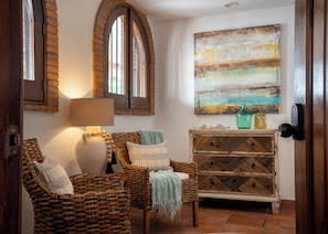 Een gezellige kamer met rieten meubels, een lamp, een houten kast en een schilderij aan de muur.