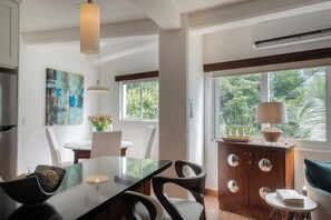 A modern dining area with a glass table, chairs, and a view of greenery outside.