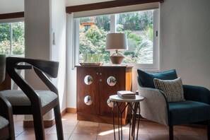 Une pièce avec un meuble en bois, une chaise, une table avec une lampe et une vue sur la verdure à l’extérieur.
