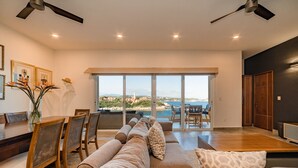 A spacious living room with a large window, a dining area, and a view of the sea. - Oceanfront Oasis Close to Beach w/ Two Pools (Huatulco)