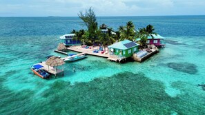 Um resort em uma ilha tropical com águas turquesa cristalinas, um píer e várias bangalôs sobre a água com telhados de palha.