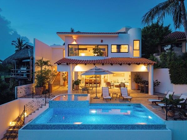 Una casa a due piani con piscina, area salotto esterna e una scala che conduce al livello superiore.