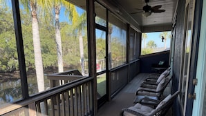 A covered porch with wicker chairs and a view of palm trees.