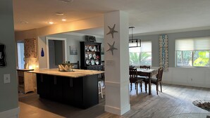 A modern kitchen with a central island, a dining area with a wooden table and chairs, and a living space with a glass coffee table.