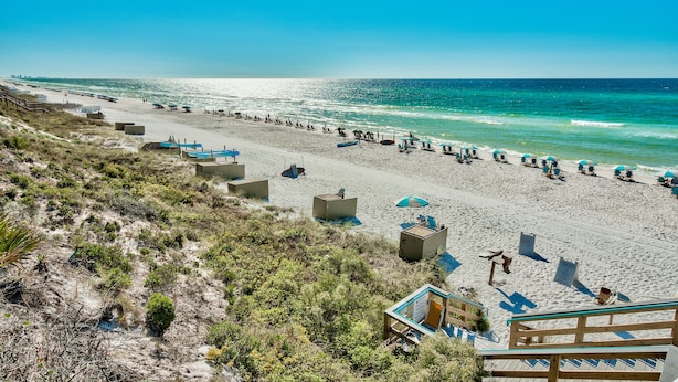 A beach with a wooden walkway leading down to the shore, beach chairs, umbrellas, and a lifeguard tower.