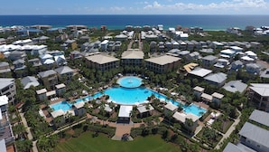 A resort with a central pool surrounded by villas, a well-maintained lawn, and a view of the ocean.