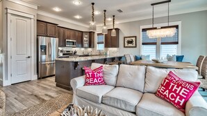 A modern kitchen with stainless steel appliances, a dining area with a wooden table, and a cozy seating area with a beige sofa and decorative pillows.