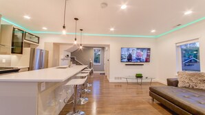 Een moderne keuken met een centraal eiland, een eethoek met een glazen tafel, en een woonkamer met een bank en televisie.