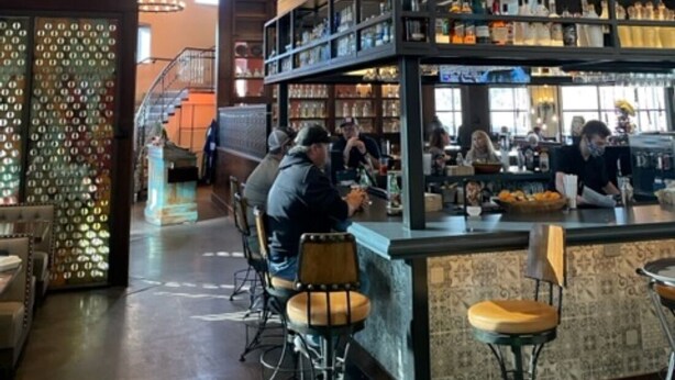 Een bar met verschillende zithoeken, een trap en diverse flessen op planken.